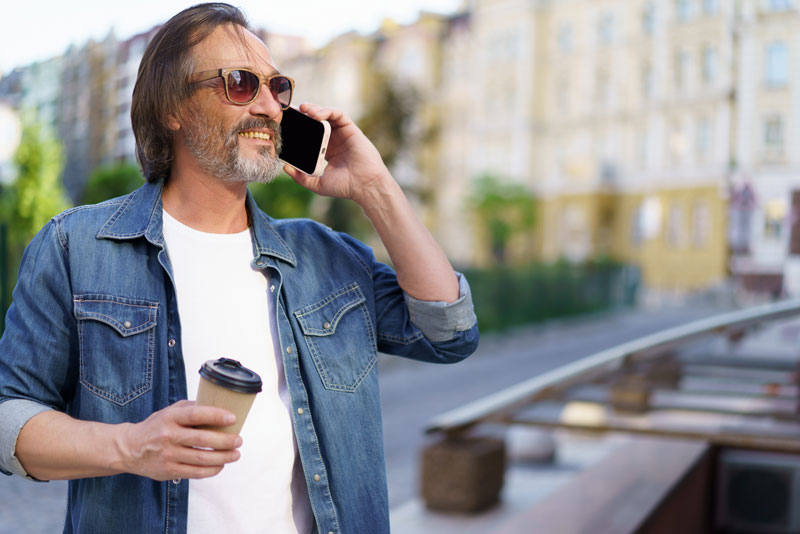 a dental implant candidate smiling as he talks on his cellphone because he can get treated with dental implants.